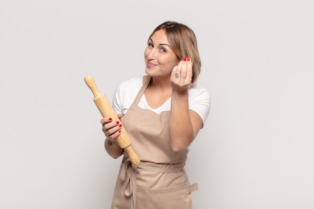 Young blonde woman making capice or money gesture, telling you to pay your debts!