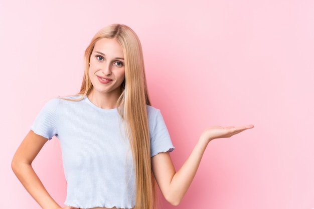 Young blonde woman on pink showing a copy space on a palm and holding another hand on waist.