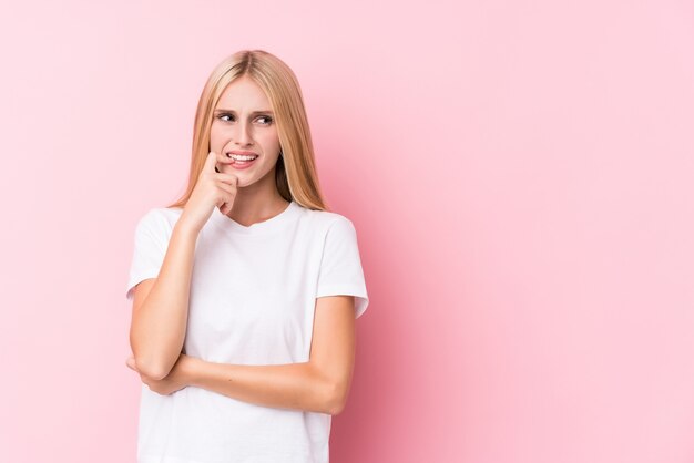 Young blonde woman on pink wall relaxed thinking about something looking at a copy space.