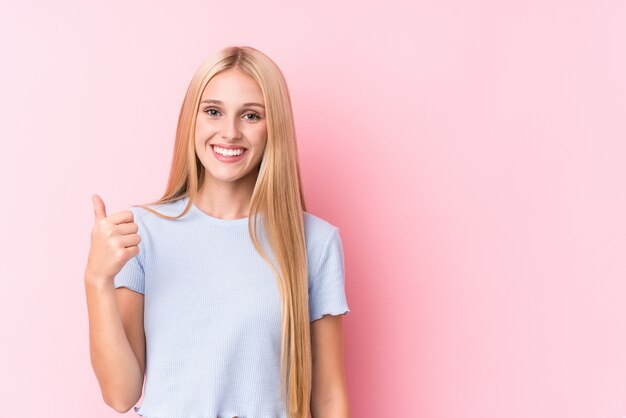 Young blonde woman on pink wall smiling and raising thumb up