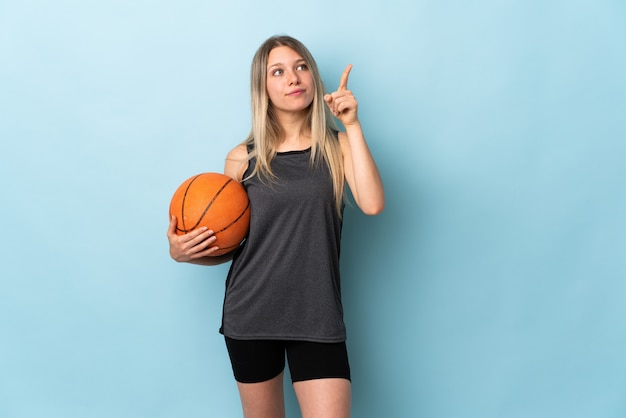 Young blonde woman playing basketball isolated on blue wall