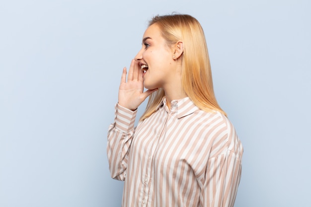 young blonde woman profile view, looking happy and excited, shouting and calling to copy space on the side