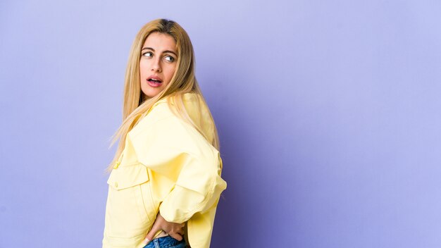 Young blonde woman on purple wall suffering a back pain.