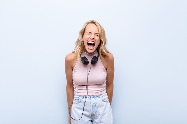 Young blonde woman shouting aggressively, looking very angry, frustrated, outraged or annoyed, screaming no listening music