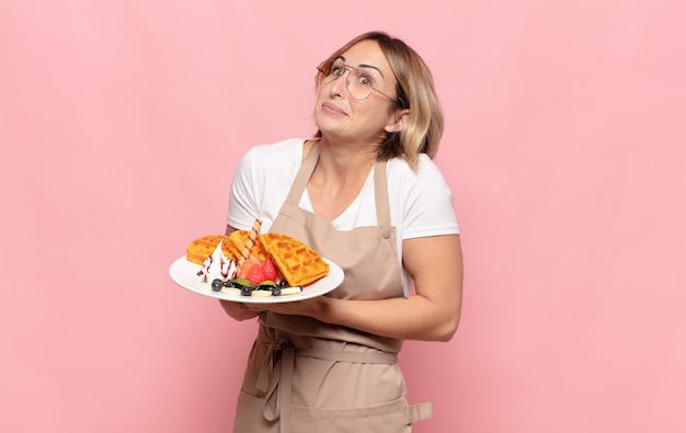 Young blonde woman shrugging, feeling confused and uncertain, doubting with arms crossed and puzzled look