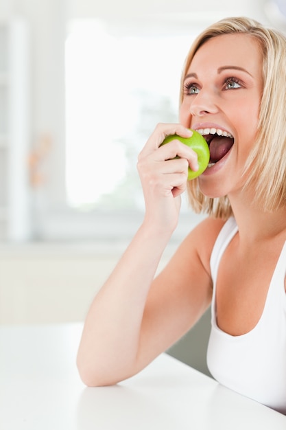 Young blonde woman sitting at table eating an apple