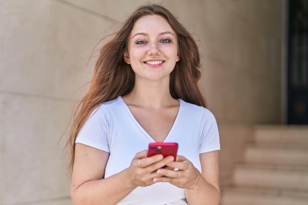 Young blonde woman smiling confident using smartphone at street