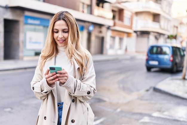 Young blonde woman smiling confident using smartphone at street