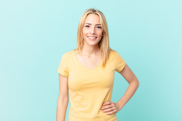 Photo young blonde woman smiling happily with a hand on hip and confident