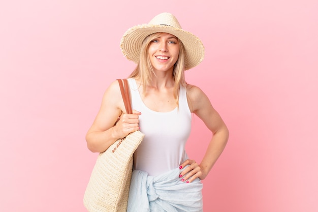 Young blonde woman smiling happily with a hand on hip and confident