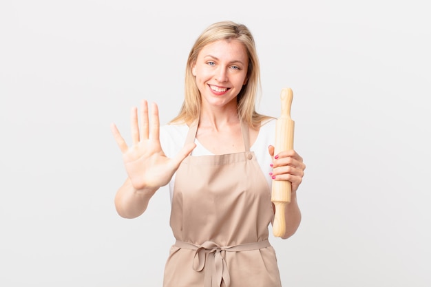 Young blonde woman smiling and looking friendly, showing number five. baker concept