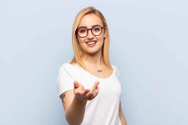 young blonde woman smiling, looking happy, confident and friendly, offering a handshake to close a deal, cooperating