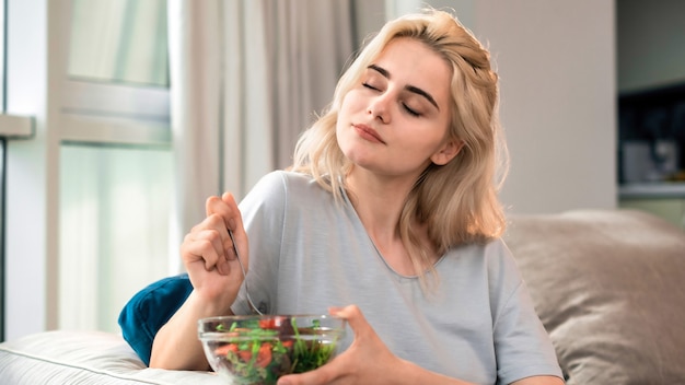 Young blonde woman on a sofa with healthy salad