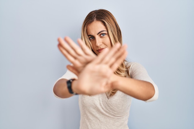 Young blonde woman standing over isolated background rejection expression crossing arms and palms doing negative sign, angry face