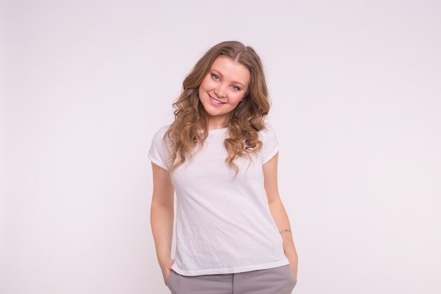 Young blonde woman standing with hands in pockets wearing white shirt.