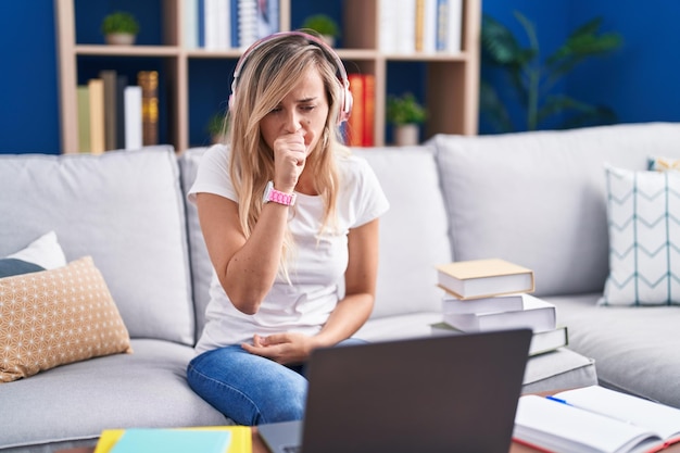 Young blonde woman studying using computer laptop at home feeling unwell and coughing as symptom for cold or bronchitis health care concept