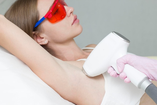 A young blonde woman undergoes the procedure of laser hair removal of her armpits in a beauty clinic