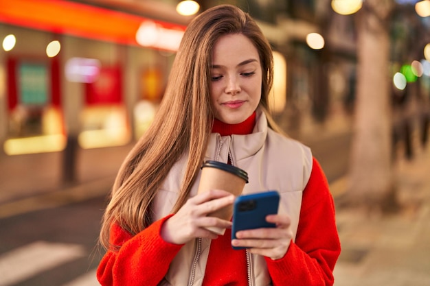 Young blonde woman using smartphone drinking coffee at street