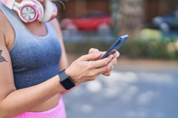 Young blonde woman wearing sportswear using smartphone at street