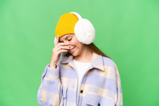 Young blonde woman wearing winter muffs over isolated chroma key background laughing