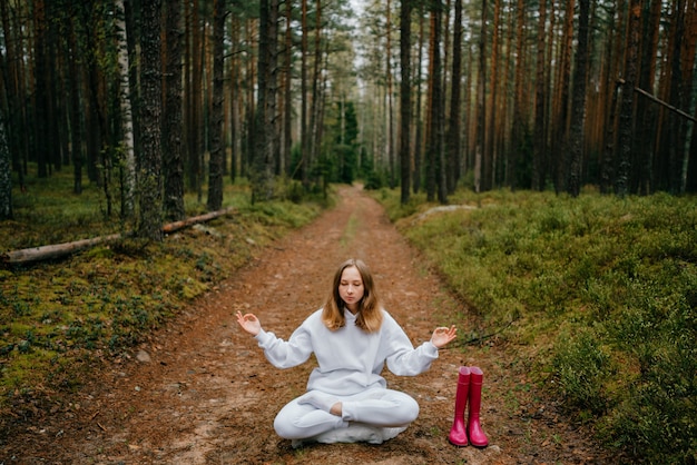 Photo young blonde woman in white tracksuit meditates in the forest