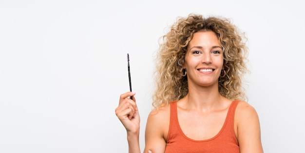 Young blonde woman with curly hair applying mascara with cosmetic rush