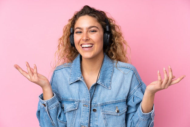 Young blonde woman with curly hair on pink surprised and listening music