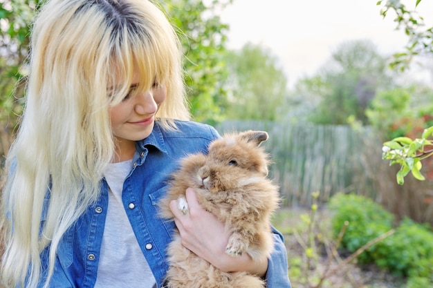 Young blonde woman with decorative rabbit in the spring garden