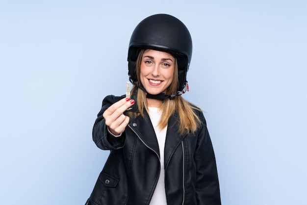 Young blonde woman with a motorcycle helmet and a key over isolated blue wall