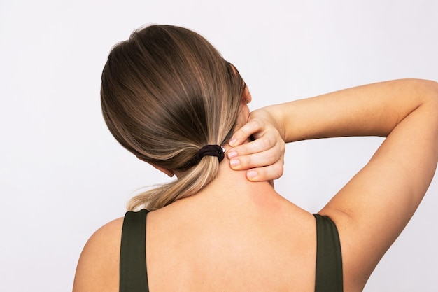 A young blonde woman with a neck pain holding her neck with hand Rear view