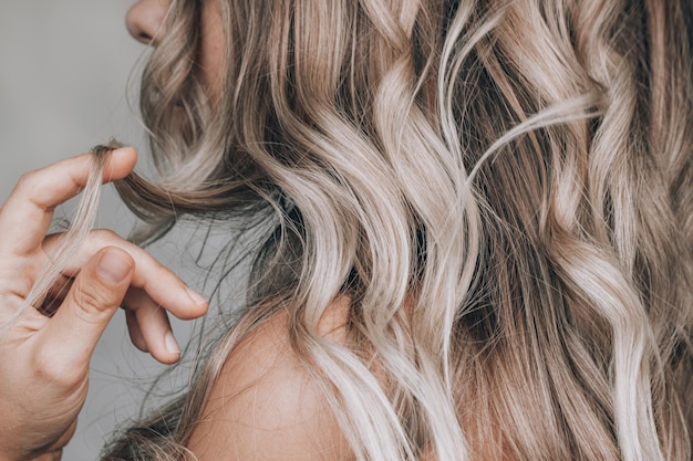 Photo a young blonde woman with the wavy hair holding a lock of hair in her hand