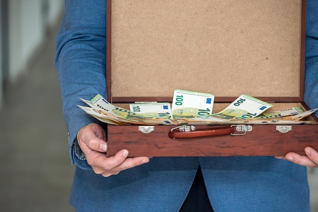 Young boss businessman in expensive suit with tie holds suitcase with euro banknotes The concept of the euro in a suitcase for a man with the tax