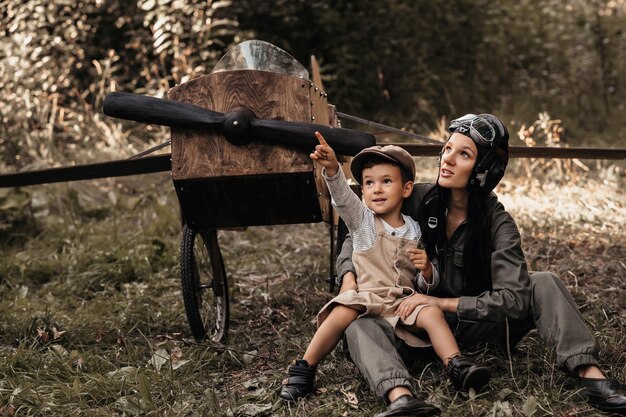 A young boy aviator together with his mother aviator in a homemade airplane in a natural landscape point a finger at the sky The authentic mood of the picture Cartography Vintage