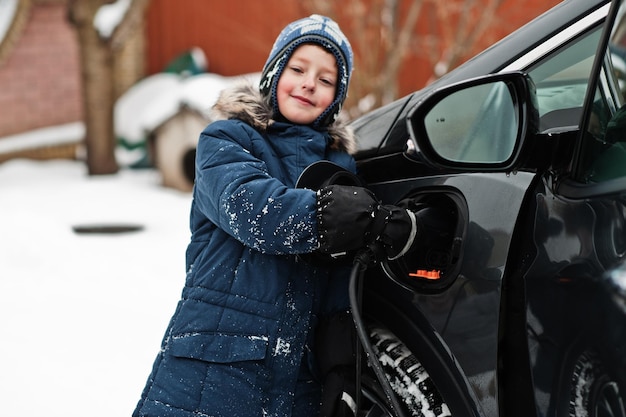 Young boy charging electric car in the yard of house at winter