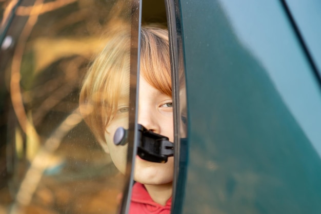 A young boy of eight or ten years old sits in a car in front of the halfopen glass Car travel train concept Redhaired boy Stuffiness in the car airing