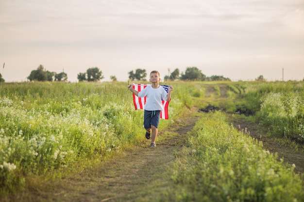 Young boy  holding an American flag at sunset in field