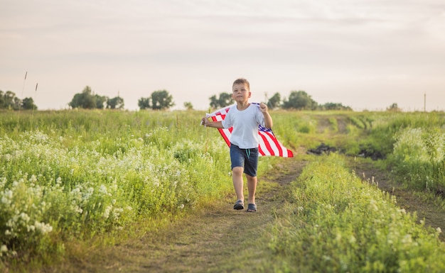 Young boy holding an American flag at sunset in field