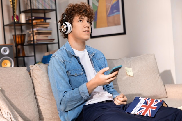 A young boy holding a phone in his hand a teenager is doing his homework while listening to music