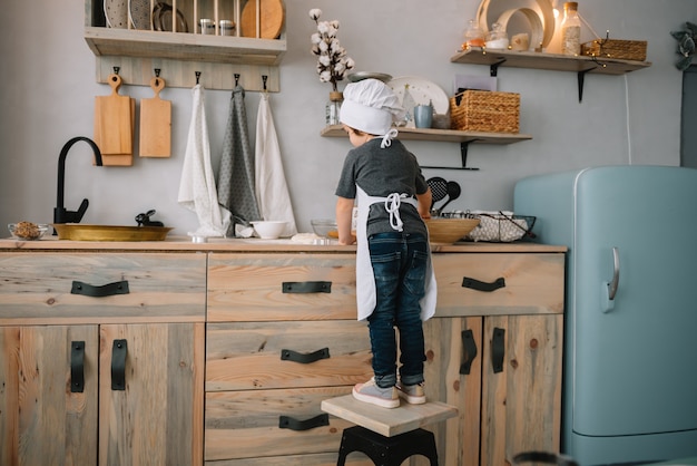 Young boy in the kitchen with chef uniform preparing dough