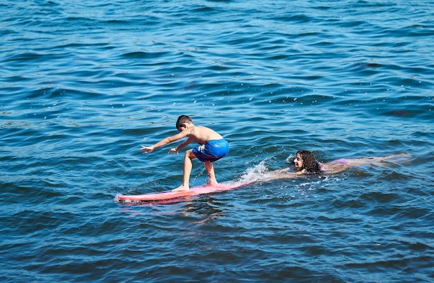 Young boy learning to surf with her older sister