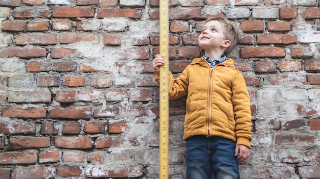 Photo young boy measuring height near brick wall