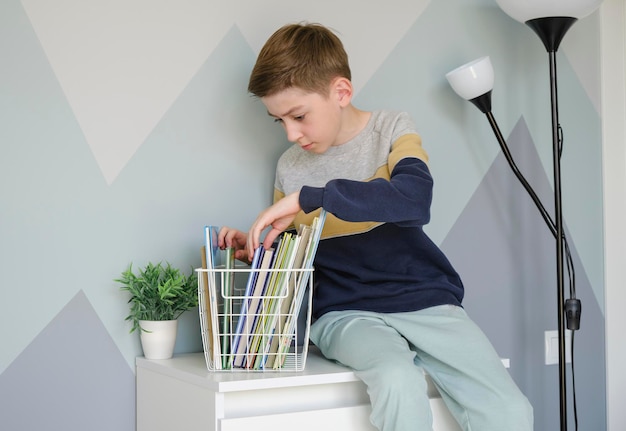 Young boy sitting and reading a book on a chest of drawers