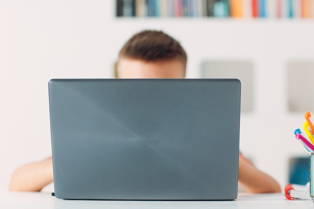 Young boy sitting at table with laptop and preparing to school online education concept