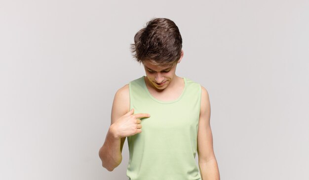 Photo young boy smiling cheerfully and casually, looking downwards and pointing to chest