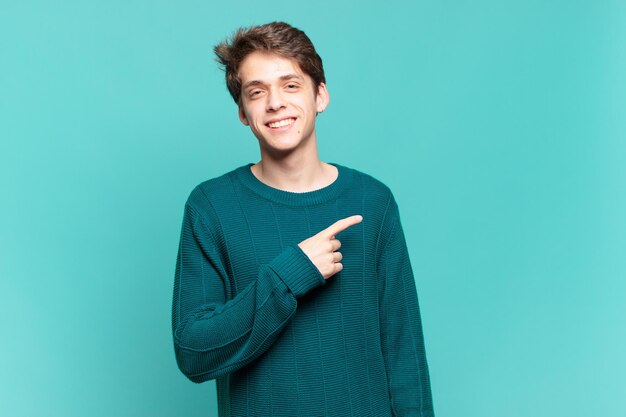 Young boy smiling cheerfully feeling happy and pointing to the side and upwards showing object in copy space