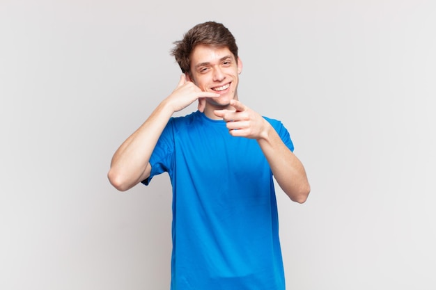 Young boy smiling cheerfully and pointing to camera while making a call you later gesture, talking on phone