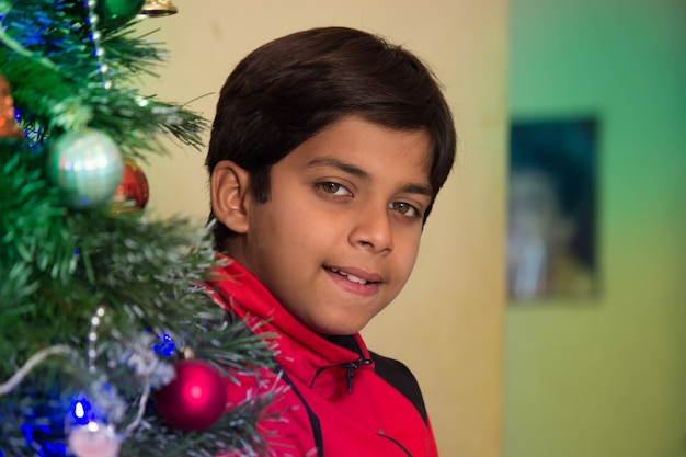 A young boy smiling in from of the Christmas tree  