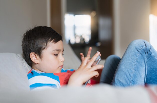 Young boy using tablet playing game on internet Kid sitting on sofa watching or talking with friend onlineChild relaxing in living room in the morning Children with New Technology concept