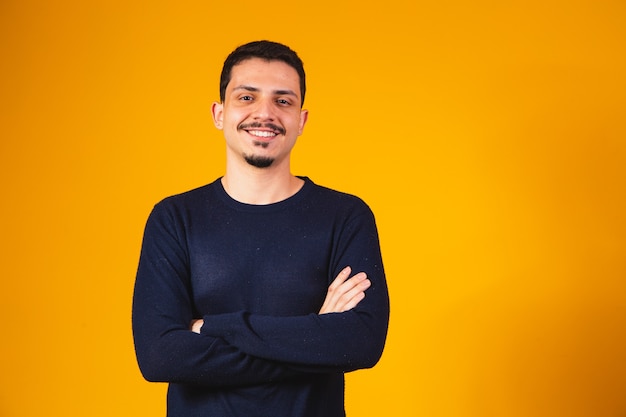 Young boy with arms crossed smiling on yellow background with free space.