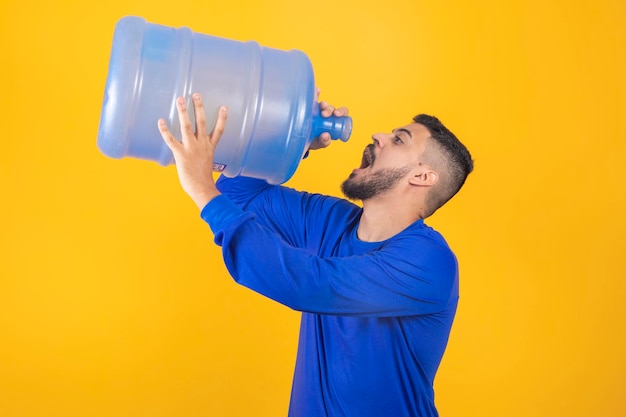 Young boy with big gallon of water drinking on yellow background